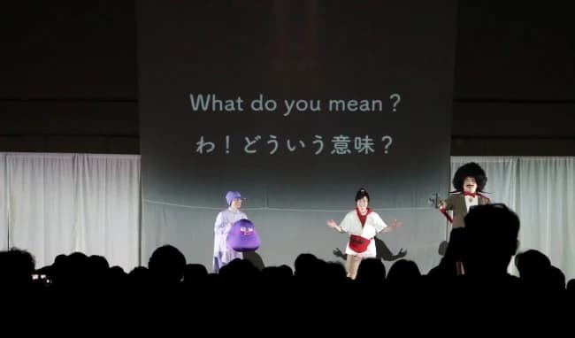 スクリーンの英語と日本語を背景に演じるマグナの登場人物たち